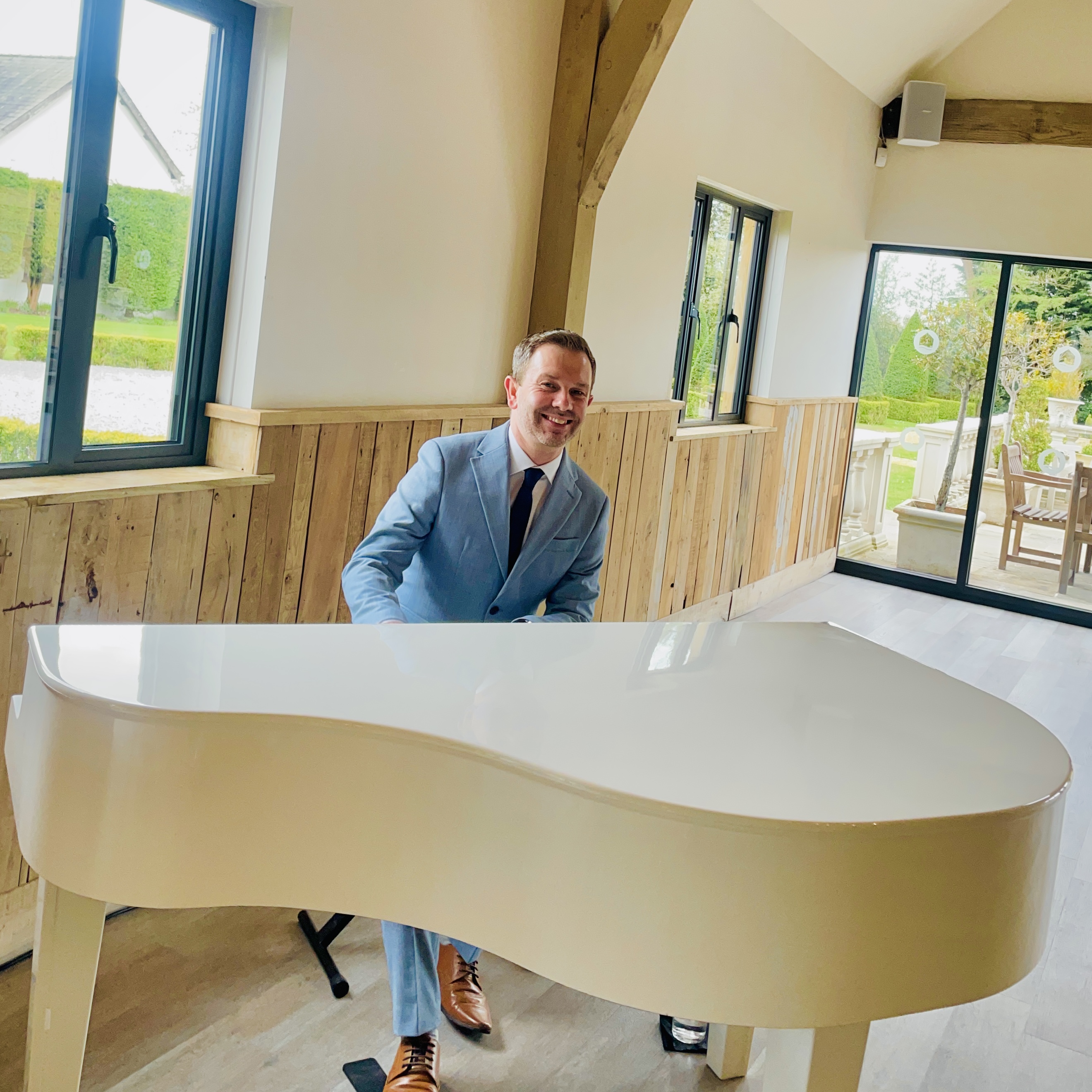 Wedding pianist Craig Smith smiles from his white piano at The River Barn